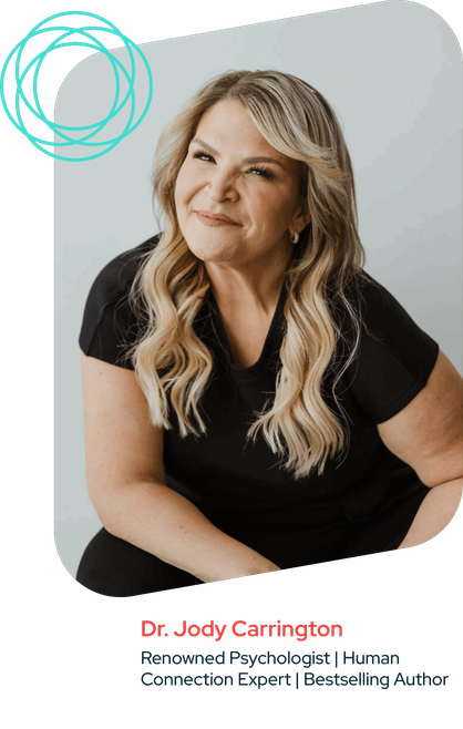 Headshot of Dr. Jody Carrington sitting in front of a solid white background. She is smiling at the camera and is wearing a black t-shirt and black pants.