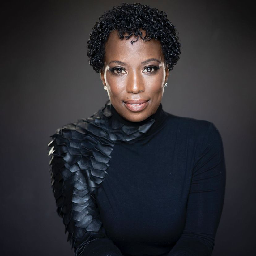 Celina Caesar-Chavannes. Headshot of Celina Caesar-Chavannes wearing a black top and standing in front of a dark grey background.