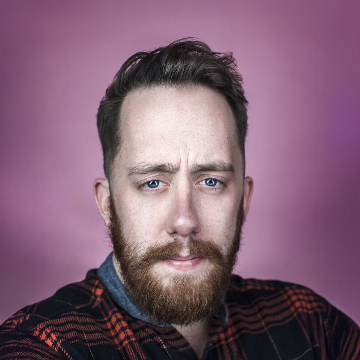 Justin Ling. Headshot of Justin Ling wearing a red plaid jacket and posing in front of a pink backdrop.
