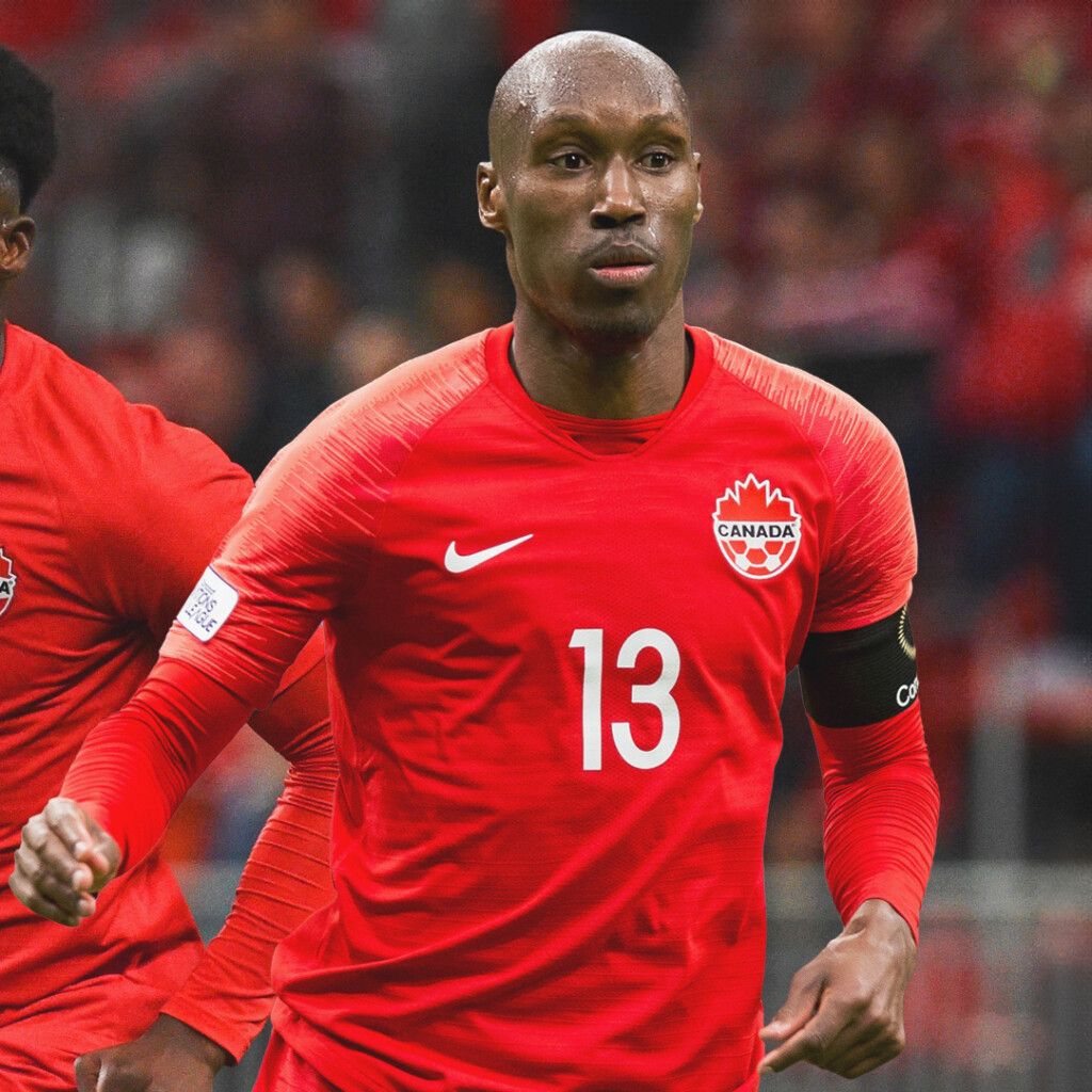 Action shot of black athlete keynote speaker, Atiba Hutchinson, on the soccer field wearing a bright red jersey with the number 13 on it.