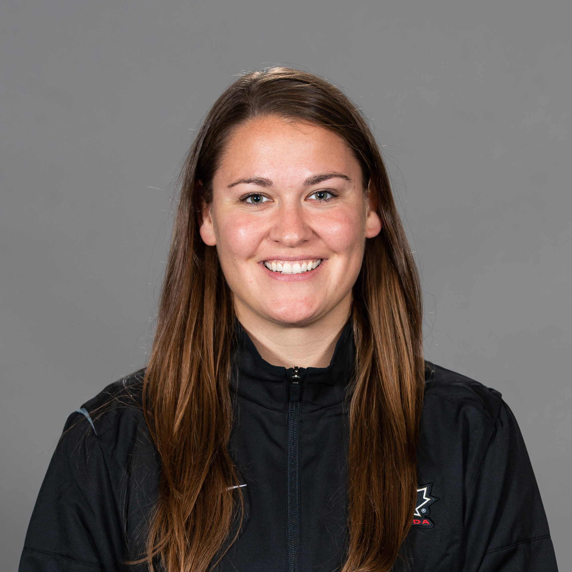 Kori Cheverie. Headshot of Kori Cheverie wearing a black zip-up jacket, posing in front of a plain grey background. She is smiling.