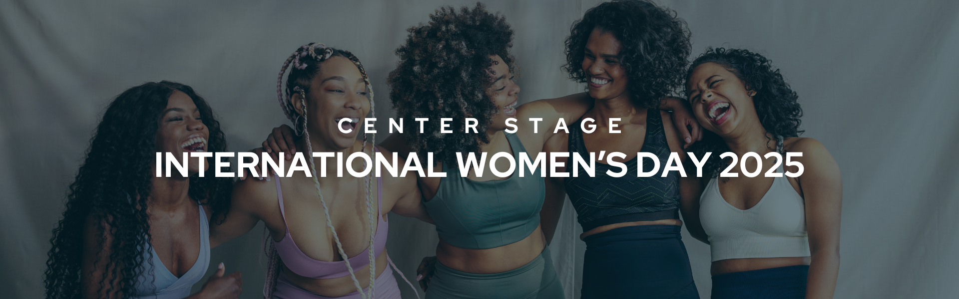 Banner that reads "Center Stage International Women's Day 2025" in bold, white text. The dark background is a photo of 5 women posing and embracing each other while laughing.