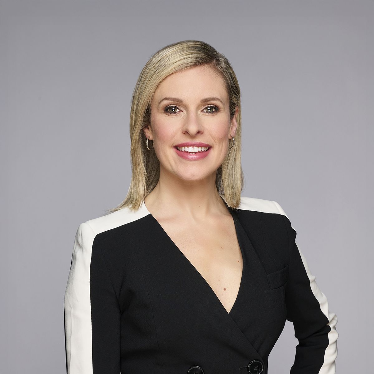 Tessa Bonhomme. Headshot of Tessa Bonhomme wearing a black and white top. She is posing with one hand on her hip and she is standing in front of a grey background.
