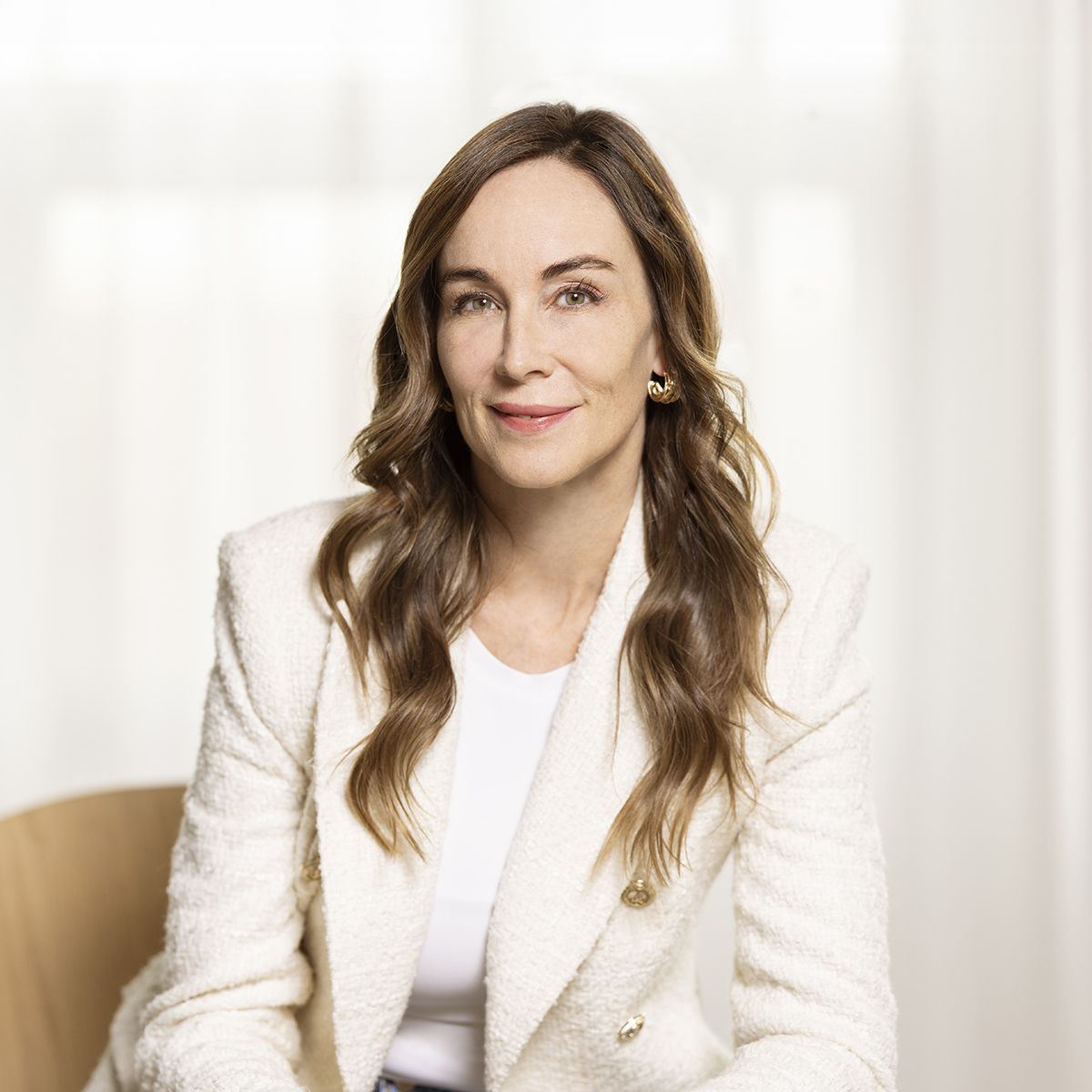 Amanda Lindhout. Headshot of Amanda Lindhout wearing a white jacket over a white shirt. She is sitting down and posing in front of a white background.