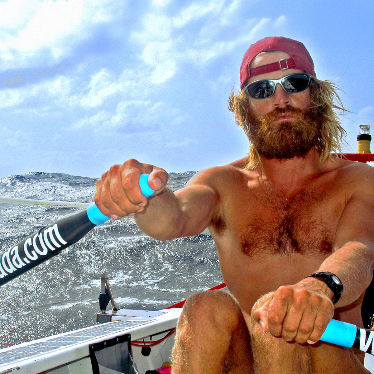 Colin Angus. Photo of Colin Angus in a rowboat on a sunny day. He is wearing a red hat and sunglasses.