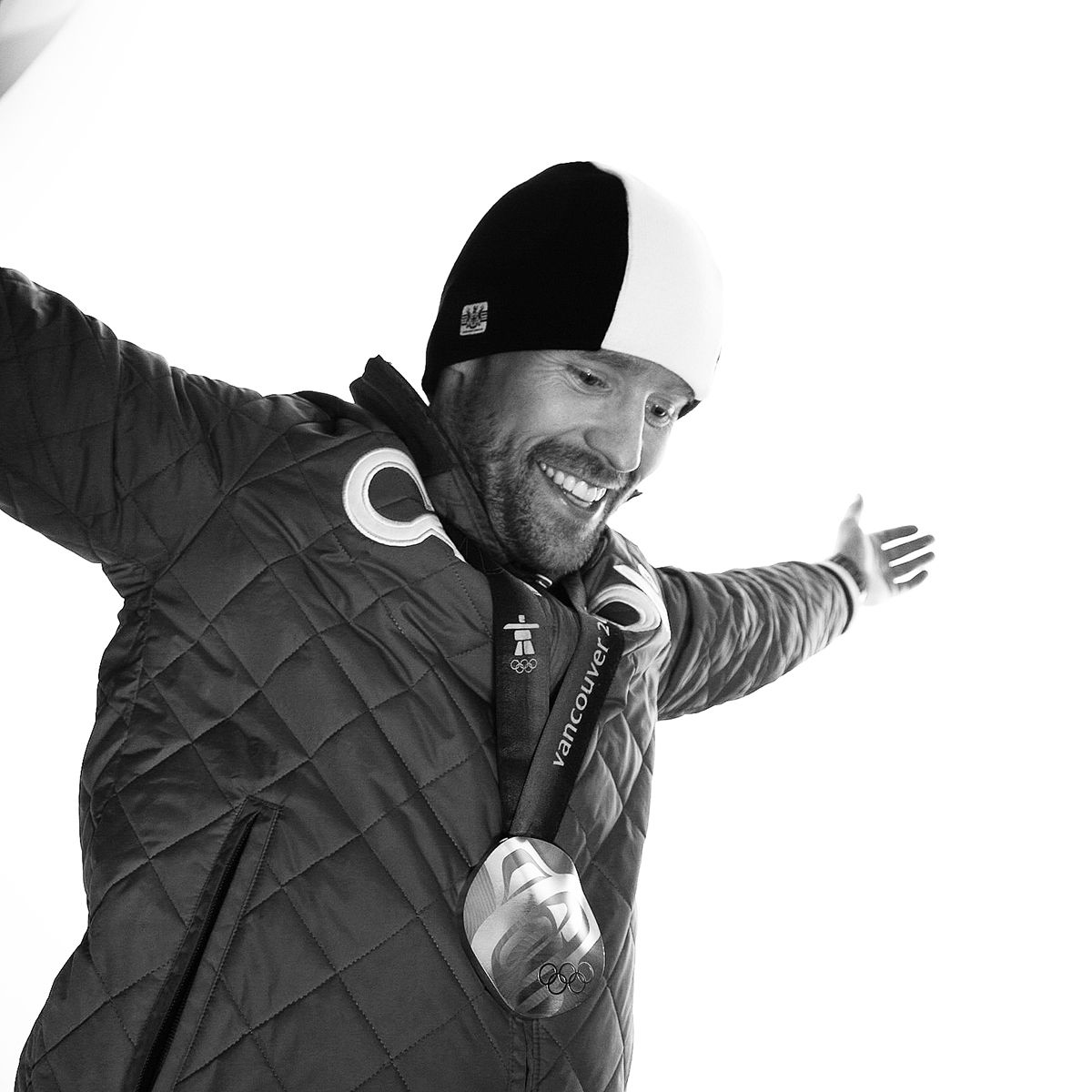 Jon Montgomery. Black and white photo of Jon Montgomery wearing a winter jacket, toque and an olympic medal.