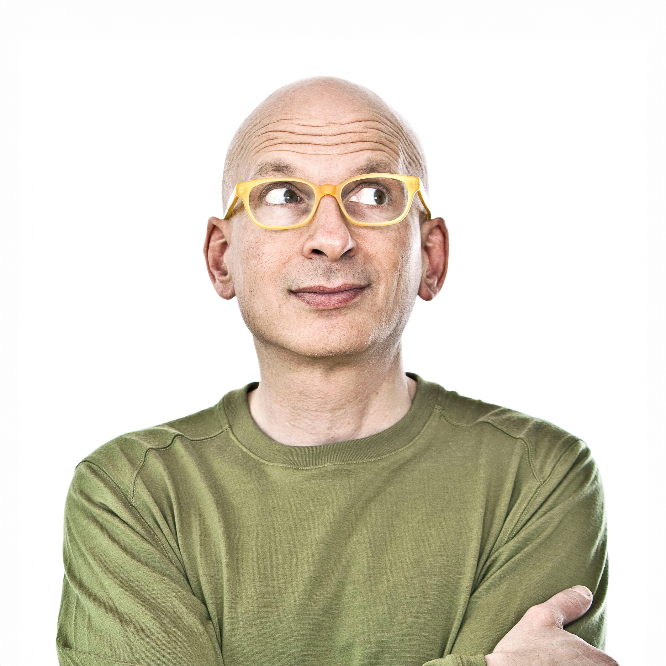 Seth Godin. Headshot of Seth Godin wearing a green shirt and glasses. He is posing with his arms crossed and standing in front of a bright white backdrop.