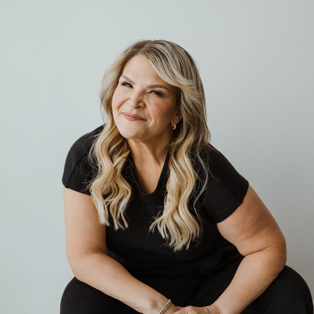 Headshot of Dr. Jody Carrington sitting in front of a solid white background. She is smiling at the camera and is wearing a black t-shirt and black pants.