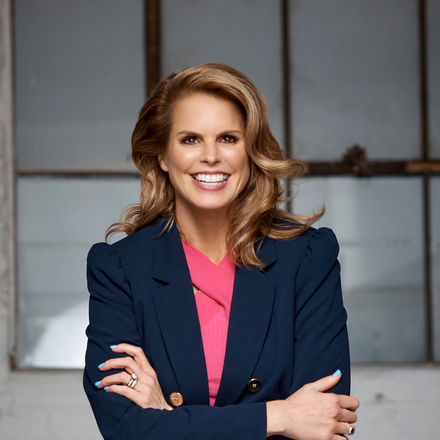 Elizabeth Lombardo. Headshot of Elizabeth Lombardo wearing a navy jacket over a pink shirt. She is posing in front of a blurred background.