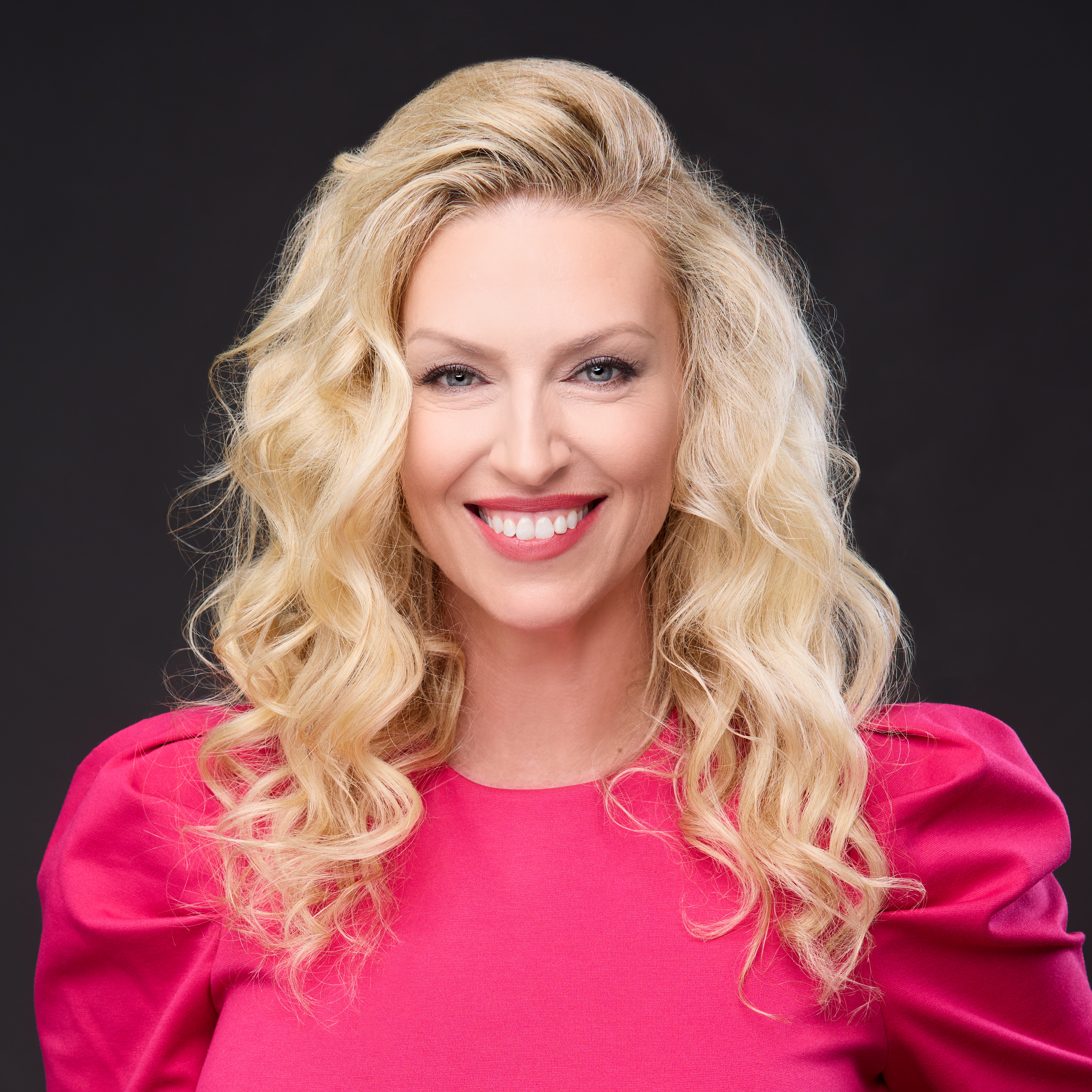 Sara Ross' headshot in front of a solid black background. She is smiling and is wearing a hot pink blouse.