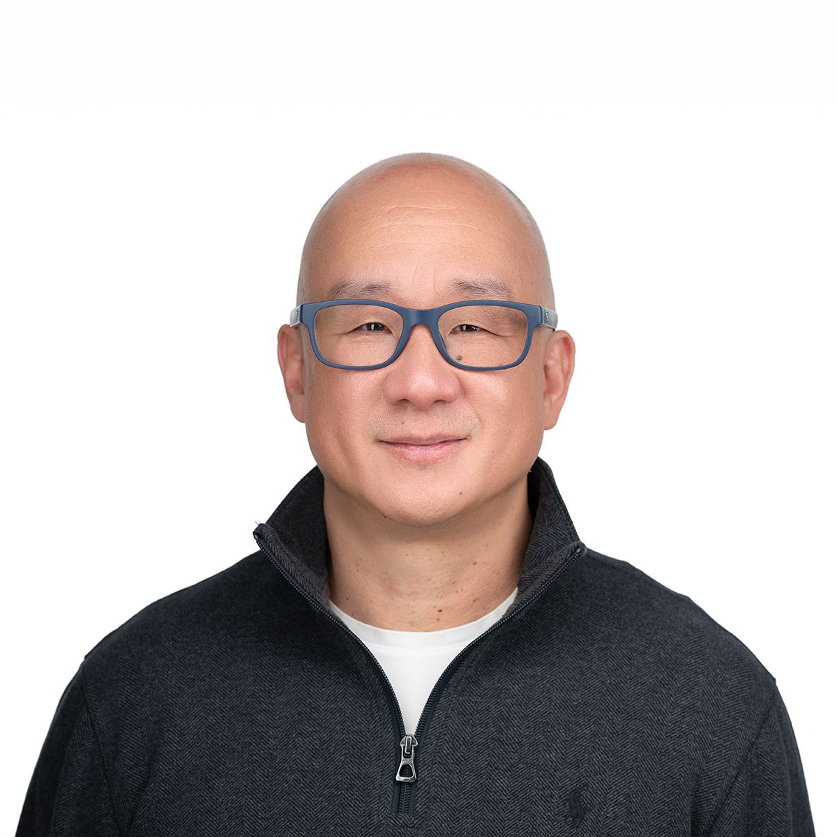 Rocky Ozaki. Headshot of Rocky Ozaki wearing a black zip-up sweater over a white t-shirt. He is posing in front of a bright white backdrop.
