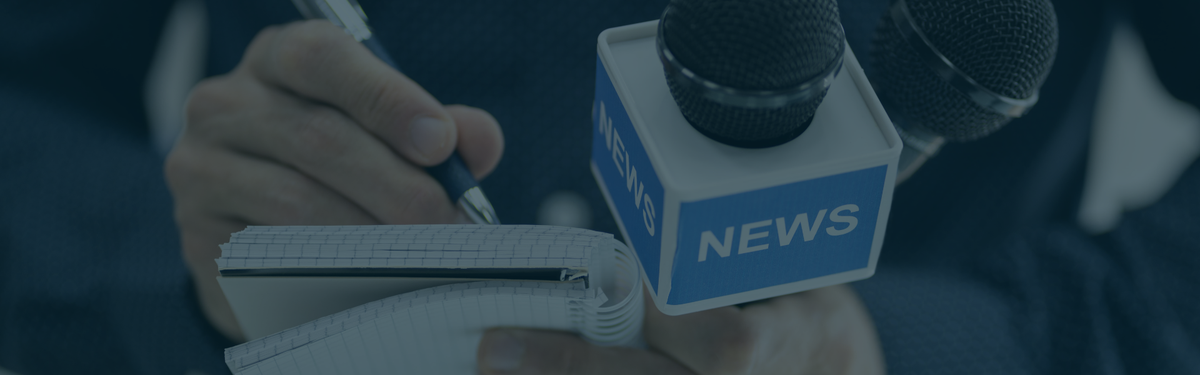Close up image of a journalist writing on a notepad with a pen. They are holding a microphone, with the word "NEWS" on it, in the other hand.