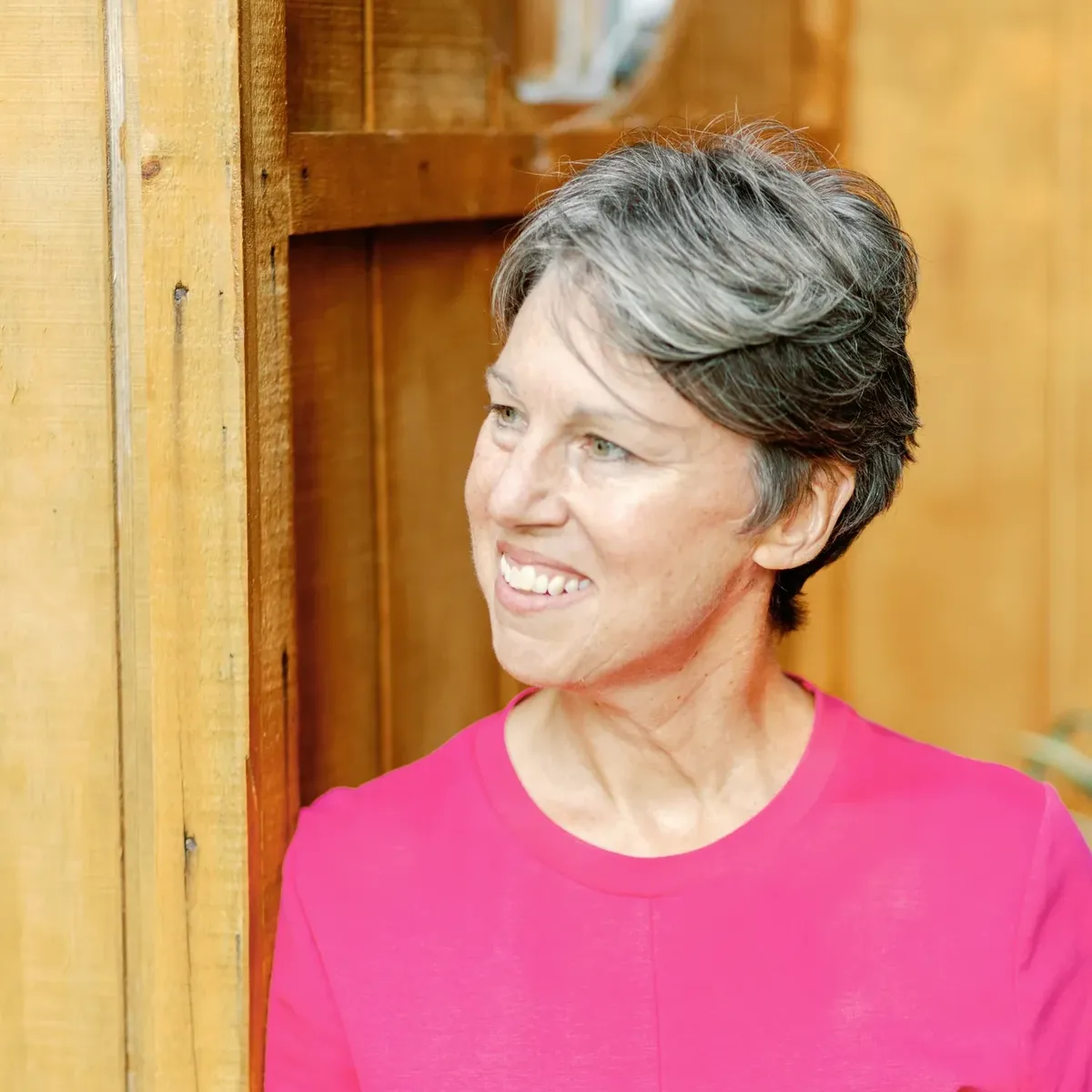 Headshot of Dr. Stephanie Nixon smiling and leaning against a wooden wall. She is wearing a bright pink t-shirt.
