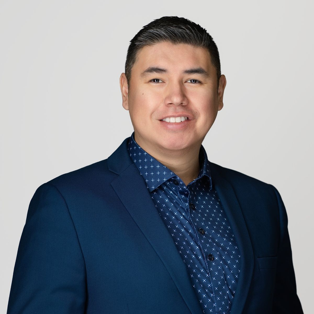 Professional headshot of Kendal Netmaker standing in front of a white background, smiling, and wearing a navy blue shirt and blazer.