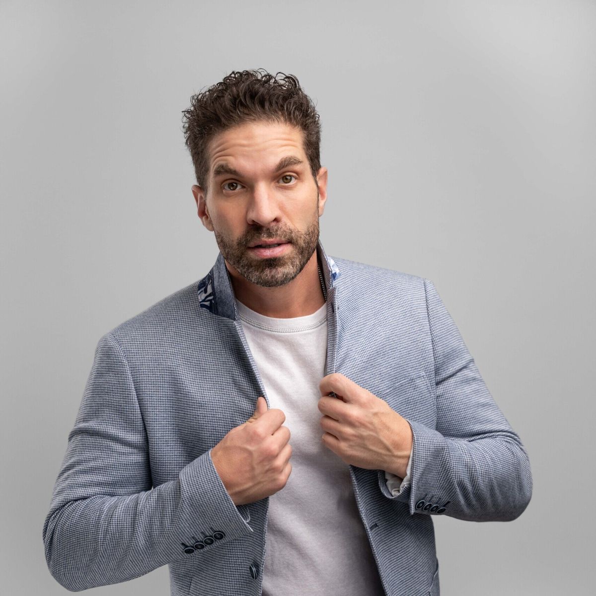 Professional headshot of Rory Gardiner in front of a grey backdrop. He is wearing a white t-shirt underneath a great blazer jacket.